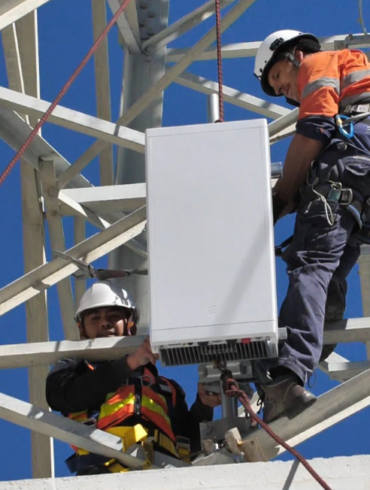 Trabajadores de telecomunicaciones instalan una antena 5G en una torre celular.