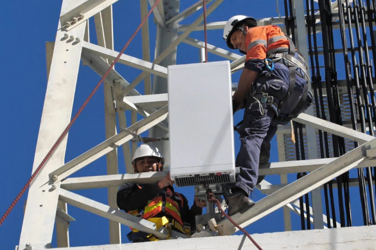 Trabajadores de telecomunicaciones instalan una antena 5G en una torre celular.